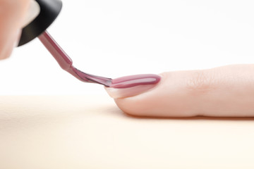 Wall Mural - manicurist applying purple nail polish on fingernail of woman on white background