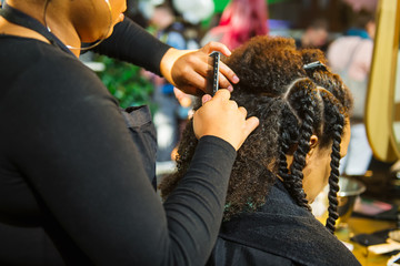 Close up african hairstylist braided hair of afro american female client in the barber salon. Black healthy hair culture and Style. Stylish therapy professional care concept. Selective focus.