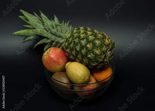 Fotografia, Obraz Pineapple orange mandarin kiwi apple with black background in vitreous bowl