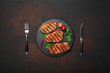 Grilled pork steaks with basil, tomatoes, knife and fork on black stone and brown rusty background