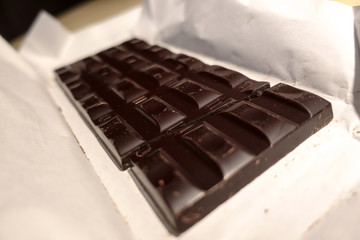 Broken black chocolate bar on white wrapping paper