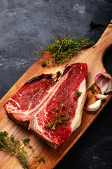 Wall Mural - T bone of beef with spices on a wooden board and black background. Raw dry aging steak 3 months.