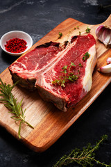 Wall Mural - T bone of beef with spices on a wooden board and black background. Raw dry aging steak 3 months.