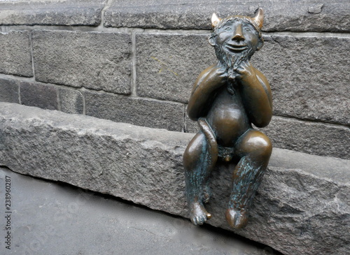 Fotografie, Obraz Small smiling devil figure made of bronze sits on a stone wall