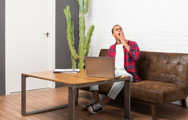 Wall Mural - African american man with laptop in the living room yawning and covering wide open mouth with hand