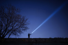 Man Pointing Flashlight To Sky At Night. 