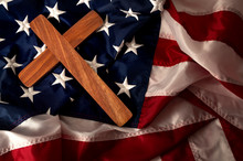 Evangelical America, Christianity, Born Again Christian And Fundamentalist Religious Right Concept With Close Up On A Wooden Cross Or Crucifix On The American Flag With Dramatic Light And Moody Tone