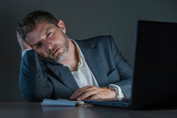 young attractive wasted and tired entrepreneur man working late night at office laptop computer desk exhausted and sleepy in financial business problem