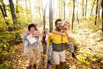 Wall Mural - Couples having piggyback ride while walking through woods in autumn. Hiking concept.