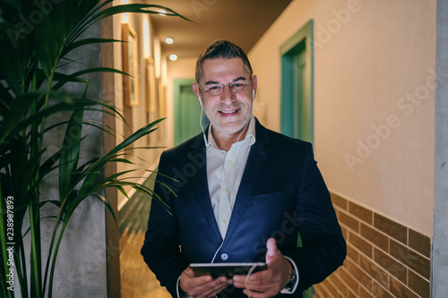 Photographie Happy Caucasian middle-aged businessman dressed smart casual using tablet for video call while standing in the hallway