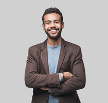 Portrait Of Handsome Smiling Young Man With Folded Arms. Laughing Joyful Cheerful Men With Crossed Hands Studio Shot. Isolated On Gray Background