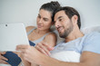 © goodluz - Attractive couple reading and relaxing in bed with book and tablet