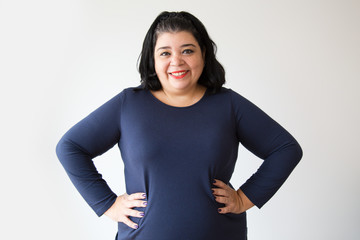 Smiling overweight Hispanic woman posing with hands on hips. Successful adult woman standing with akimbo gesture. Isolated on white. Success concept