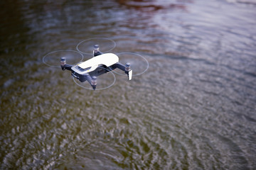 View from above on a small smart quadcopter hovering in the air over a water surface. Circles on water caused by air flow. Drone sensors testing.