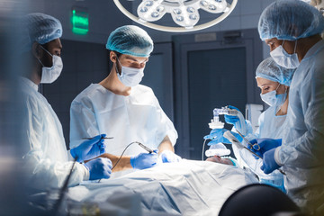 Wall Mural - Blurred figures of surgeons in medical uniforms performing surgery in operation theatre, copyspace