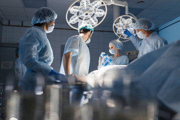 Wall Mural - Blurred figures of surgeons in medical uniforms performing surgery in operation theatre, copyspace