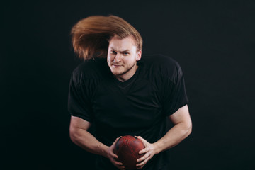 Wall Mural - Healthy american football goalkeeper holding ball in arms looking at camera with cheerful and confident expression posing isolated on black background