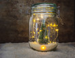 View of a jar with snow and a green Christmas tree decoration and Christmas lights on white snow and a wooden rustic background with copy space. Christmas interior decoration or design concept