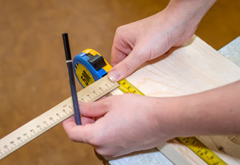 Construction work, a man measures the distance on a wooden board with a measuring tape, a carpenter at work, hands of a worker...