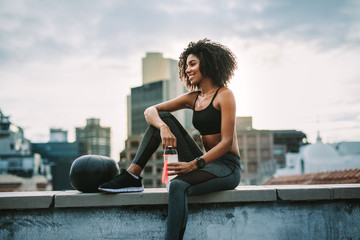 Canvas Print - Fitness woman sitting on rooftop taking break from workout