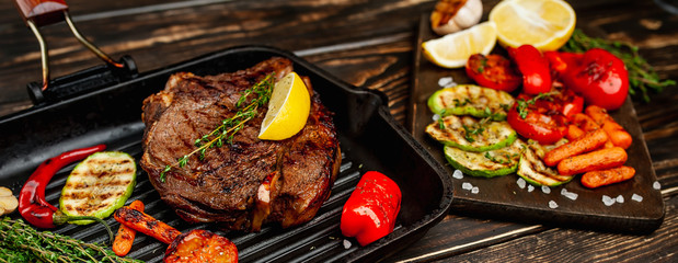 Wall Mural - steak in a grill pan, next to chopped vegetables, lemon, red pepper, garlic and seasonings on a dark rustic background