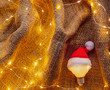 Bulb in Santa Claus hat with Christmas Lights around on jute backgroun