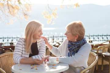 Conversation of two beautiful women in street cafe. Mother and her adult daughter have dialogue outdoor. Happy senior woman and young girl are smiling. Concept of support, care, family love, relations