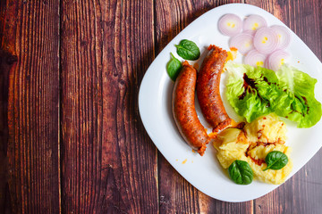 Sausages with green salad, balsamic vinegar, mashed potatoes, red onions, on a wooden rustic table. blur, clean, bright, authentic, retro, contrast, top view.