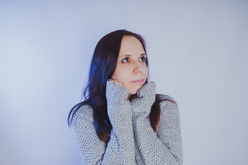 A young girl in a sweater posing against a gray wall. Woman dressed in warm sweater, street style clothing. Clean skin, long hair