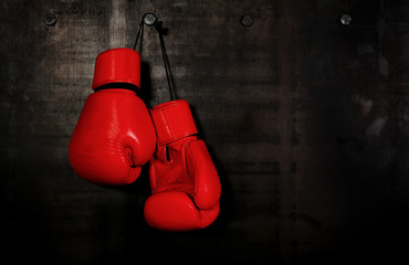 Red leather boxing gloves hanging on black wall