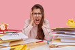 © wayhome.studio  - Photo of beautiful woman in panic, shouts from depression and frustration, has much work and deadline, feels tired, surrounded with piles of paper documents expresses negative feelings sits at desktop