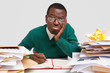 © WHstudio Leushin N - People and tiredness concept. Photo of displeased cheerless black male worker has dejected facial expression, feels fatigue of work, surrouded with piles of papers, isolated over white backround