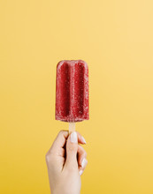 Hand Holding A Raspberry Popsicle Against A Yellow Background
