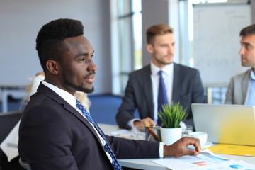 Smiling confident African businessman in a meeting with a colleagues seated at a conference table in the office.