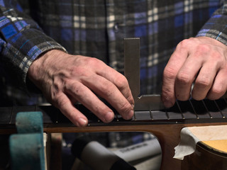 Installation frets on the neck of the guitar. Master checks the level of frets.