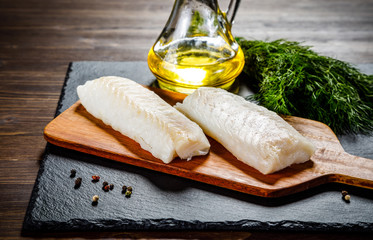 Fresh raw cod with herbs served on black stone on wooden table