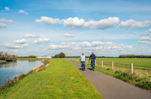 Two Unidentified People Cycle On A Bike Path At The Top Of A Dike