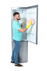 Wall Mural - Young man cleaning refrigerator with rag on white background