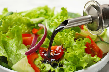 Pouring balsamic vinegar onto fresh vegetable salad in dish, closeup