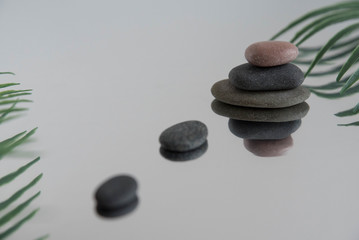 Pyramids of gray zen pebble meditation stones with green leaves on the mirror water reflection background. Concept of harmony, balance and meditation, spa, massage, relax