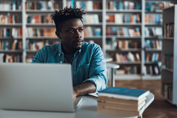 Calm Afro-American looking into the distance while sitting with laptop