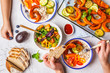 © vaaseenaa - Family eating a healthy vegetarian food. Vegan lunch table top view, plant based diet. Baked vegetables, fresh salad, berries, bread on a white background.