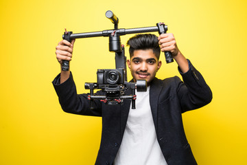 Professional indian man videographer with gimball video slr isolated on yellow background