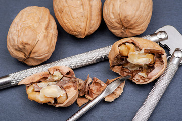 Brown premium raw organic walnuts and nutcracker in wooden bowl on natural stone background