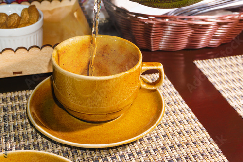 Fotografie, Obraz green tea is poured in a thin stream into a yellow cup standing on a table among the food