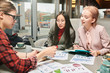 © Seventyfour - Group of young women sitting at the table in cafe and discussing different charts and graphics together in team