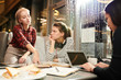 © Seventyfour - Group of female friends gathered in cafe and doing homework together, using literature books and laptop computer