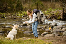 Young Girl Trains And Plays With Puppy Golden Retriever In The Wild, Next To A River.
