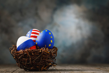 Wall Mural - Three Easter eggs in a nest painted in colors of the flags of Russia, America and European Union on a wooden table with copy space