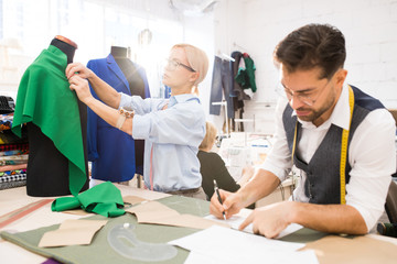 Wall Mural - Portrait of fashion designers working in atelier lit by sunlight, focus on man drawing sketches in foreground, copy space